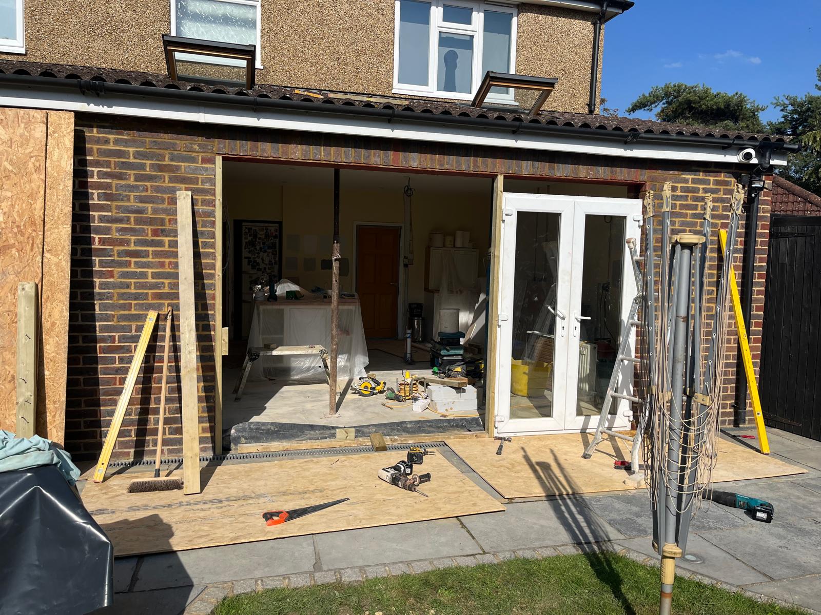 Rear wall opened up and propped during a window-to-door conversion, showing the structural work behind a new bi-fold door opening